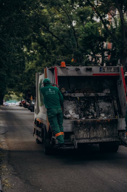 A large pile of black trash bags, filled with waste, is stacked against a tiled wall on an outdoor paved area. Some bags are torn or bursting, revealing plastic bottles and other rubbish inside. A few