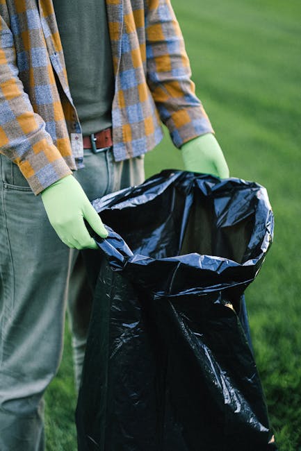 A small, older model blue pickup truck parked alongside a street with its bed and cabin overloaded with a large amount of mixed waste materials. The truck's exterior shows signs of wear, with visible